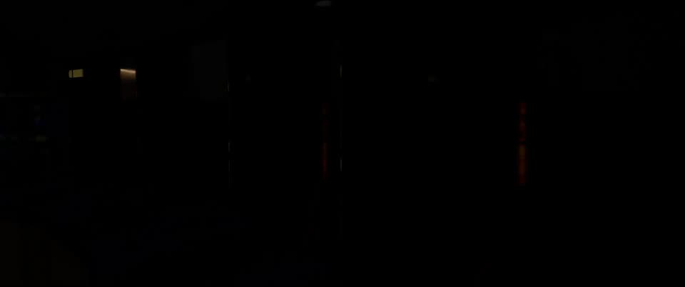 A almost completely black frame, with a few faint dim lights: a small yellow glow at upper left and two thin orange-red vertical strips in the middle and right.